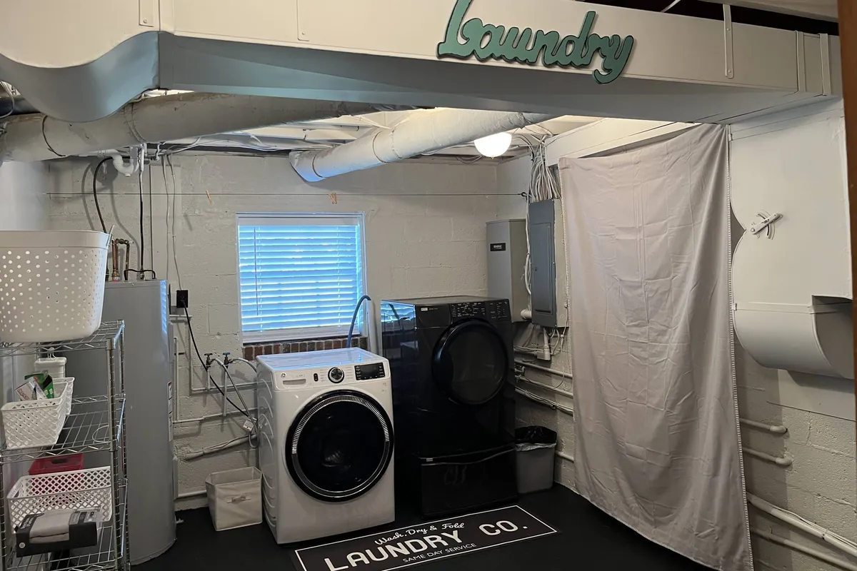 A bright, tidy laundry area featuring a front-loading washer and dryer beneath a window, with a decorative 'laundry' sign adding a homey touch. The space exudes practicality and is clearly designed for convenient clothes care and gear cleaning.