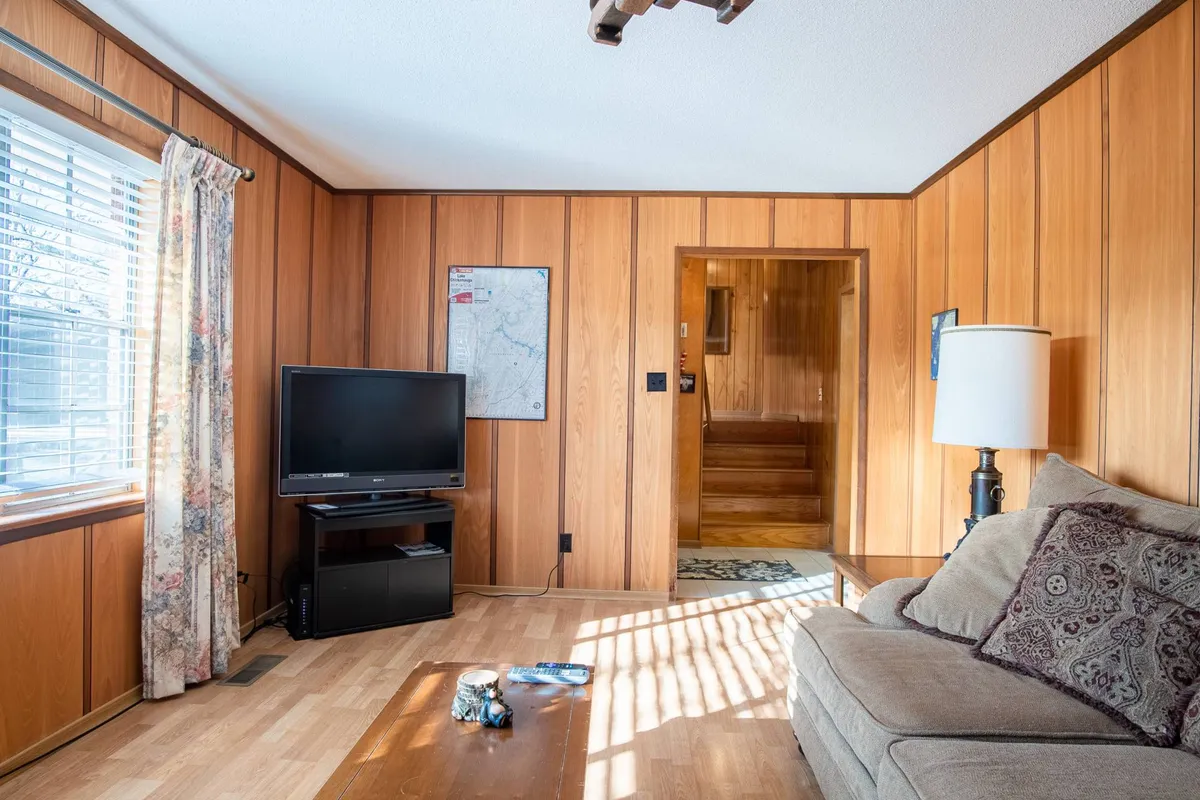 This image captures a cozy living room featuring a sofa, television, wood paneling, and a staircase. Sunlight pours in through the windows, and the space exudes warmth and comfort—ideal for group gatherings, socializing, and movie nights.