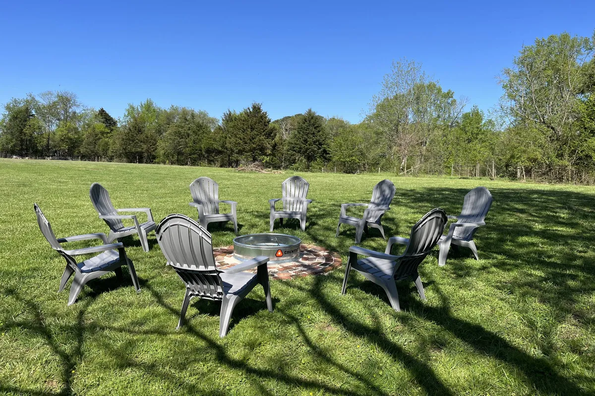 A welcoming fire pit area surrounded by classic Adirondack chairs set on open grassy land, ideal for group gatherings, storytelling, or stargazing under the night sky.