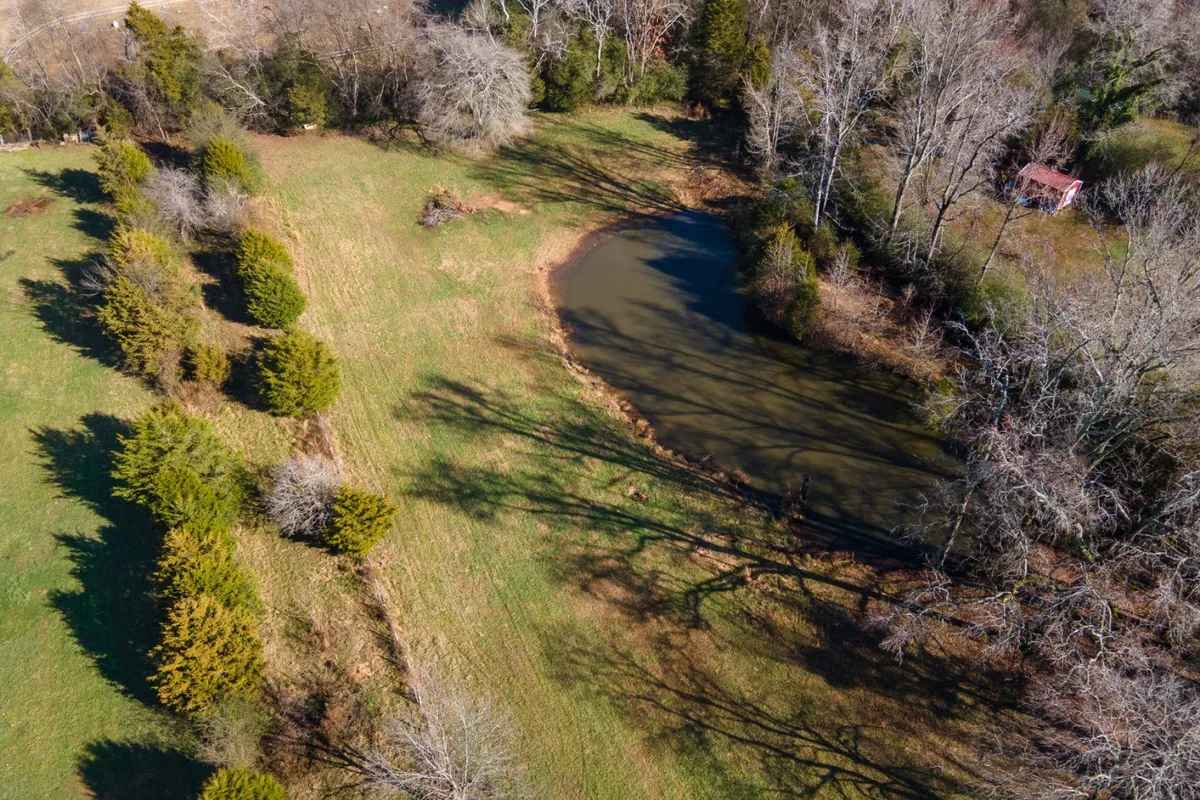 A serene pond is bordered by a tree line and open grassland, with a distant red shed adding visual interest. The peaceful natural setting invites fishing, picnicking, and quiet reflection—perfect for groups seeking more than just golf during their stay.