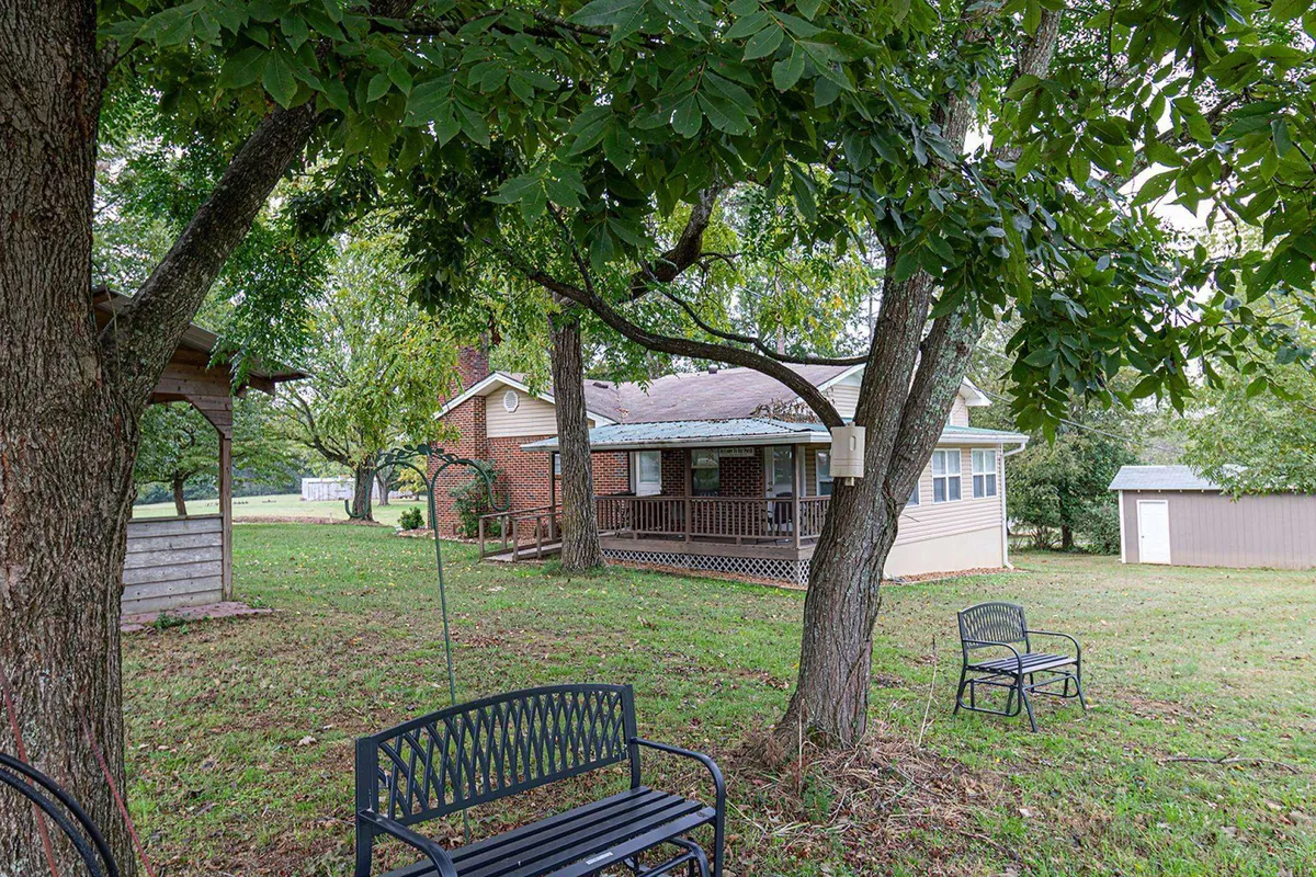This exterior shot shows the rental property, benches for outdoor relaxation, surrounding trees, and a shed. The peaceful yard invites gatherings and highlights the tranquil, welcoming atmosphere that awaits after a long day on the course.